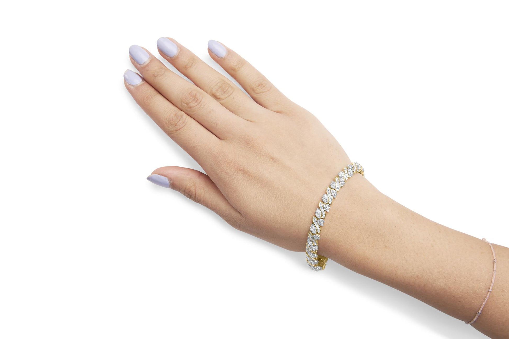 Yellow metal bracelet with round and baguette white gemstones on a model's wrist, shot from above.