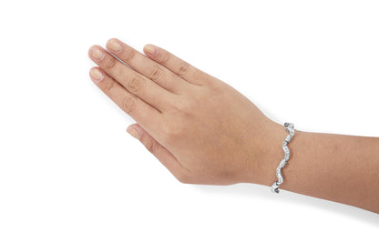 White metal bracelet with channel-set baguette white gemstones in a wavy design, shown on a model's wrist from a side angle.