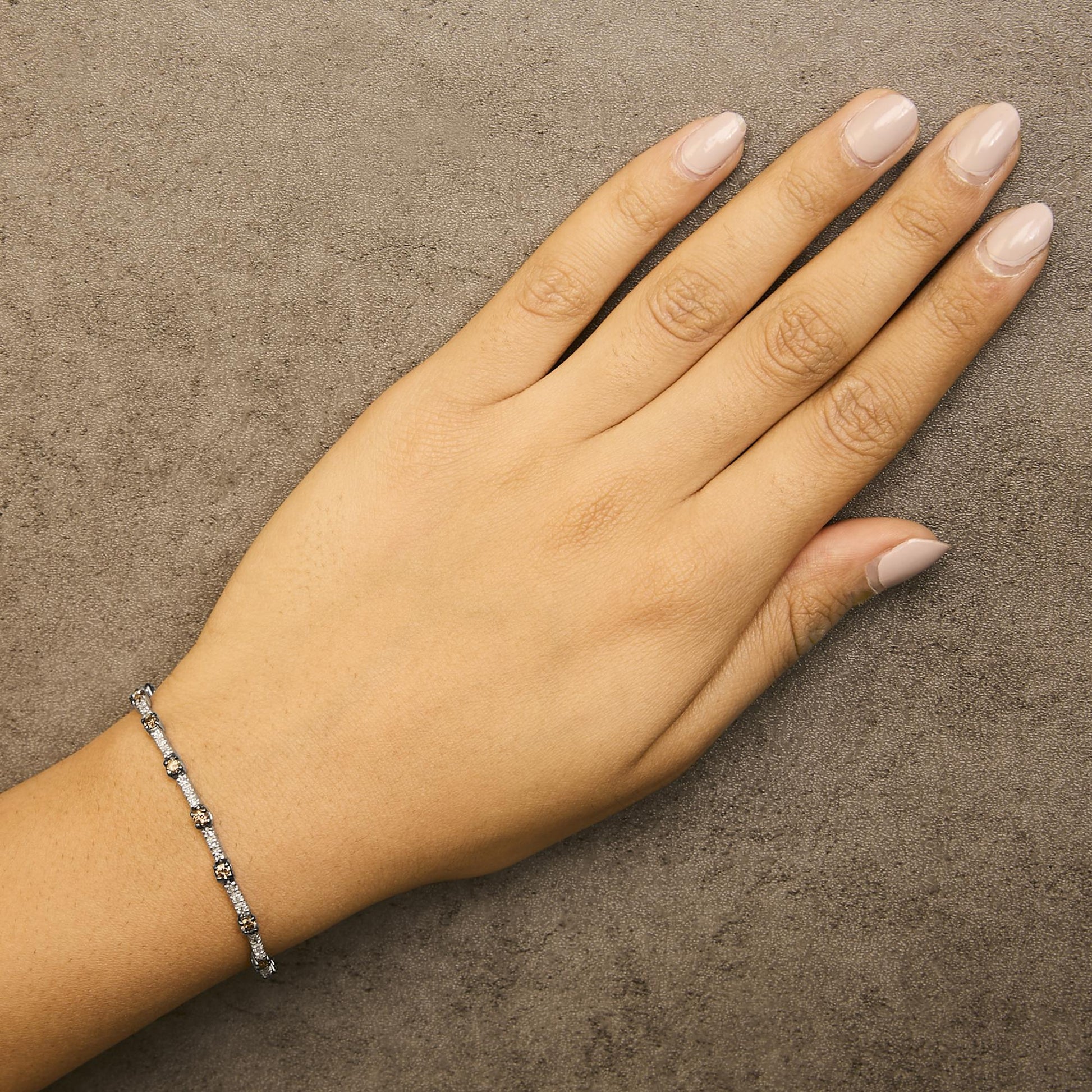 White metal bracelet with alternating white and champagne round gemstones in prong settings, shown on a model's wrist from a top-down angle.