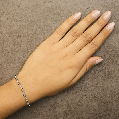 White metal bracelet with alternating white and champagne round gemstones in prong settings, shown on a model's wrist from a top-down angle.