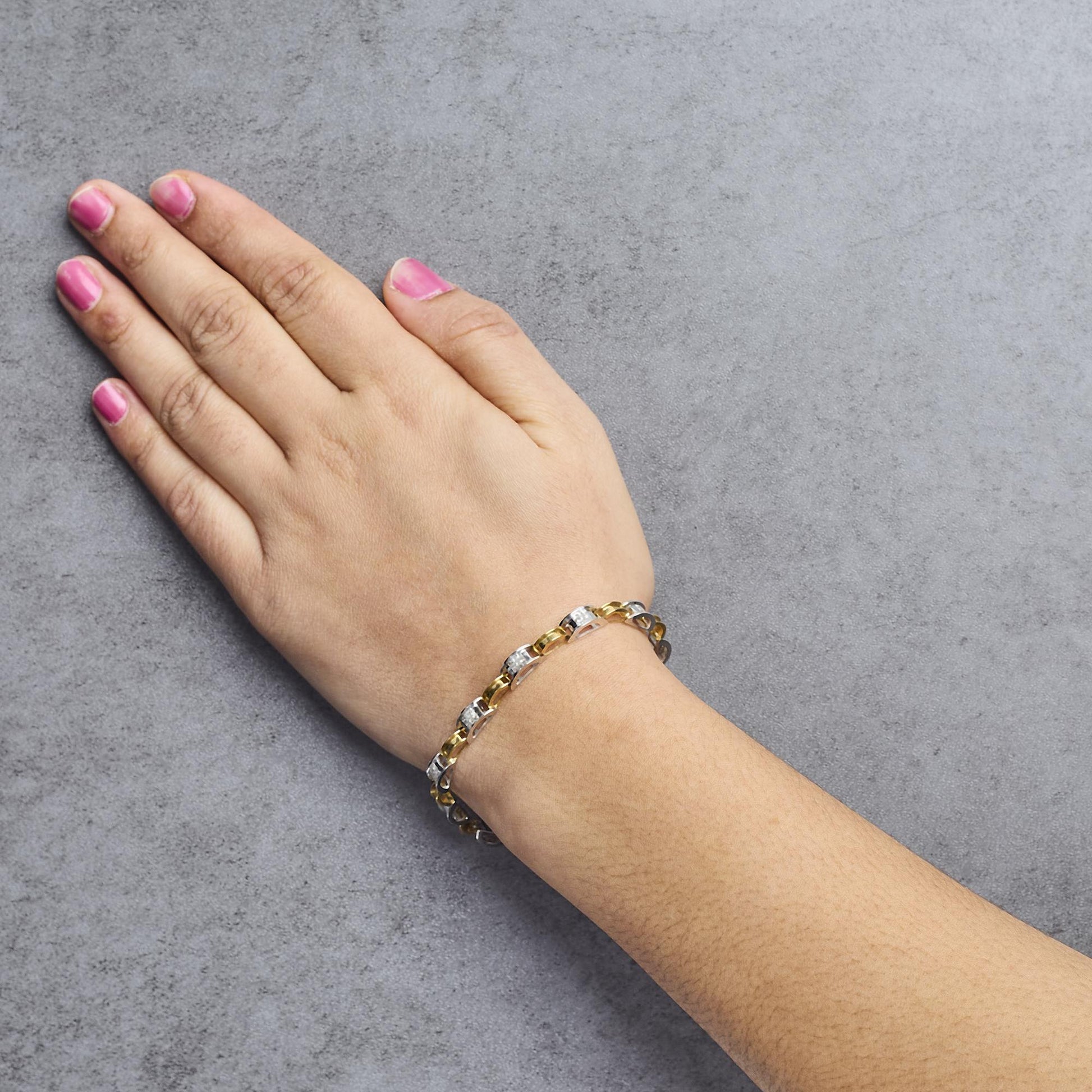 Bracelet with alternating yellow and white metal links featuring white princess-shaped gemstones in channel settings, worn on a model's wrist, top angle.