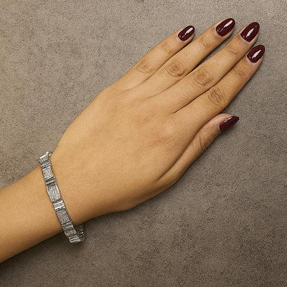 White metal bracelet with square-shaped links featuring white gemstones in an invisible setting, shown on a model’s wrist from a top-down angle.