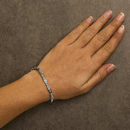 White metal bracelet with white round gemstones in prong settings and white princess gemstones in channel settings, worn on a model's wrist, angled from above.