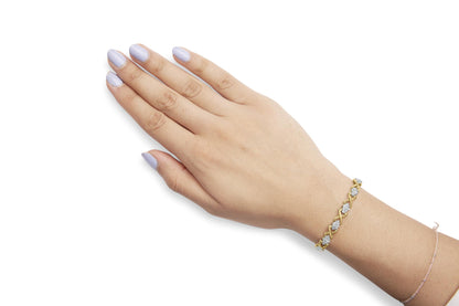Yellow metal bracelet with white round gemstones in prong settings, shown on a model's wrist from a top angle.
