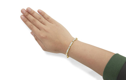 Yellow metal bracelet with white baguette and princess shape gemstones, worn on a model's wrist, shown from a top-side angle.