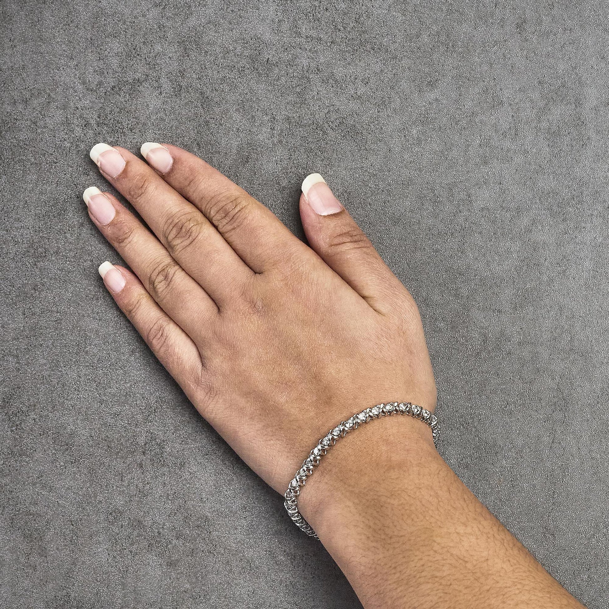 White metal bracelet with round white gemstones in two-prong settings, shown worn on a model's wrist from a top-down angle.