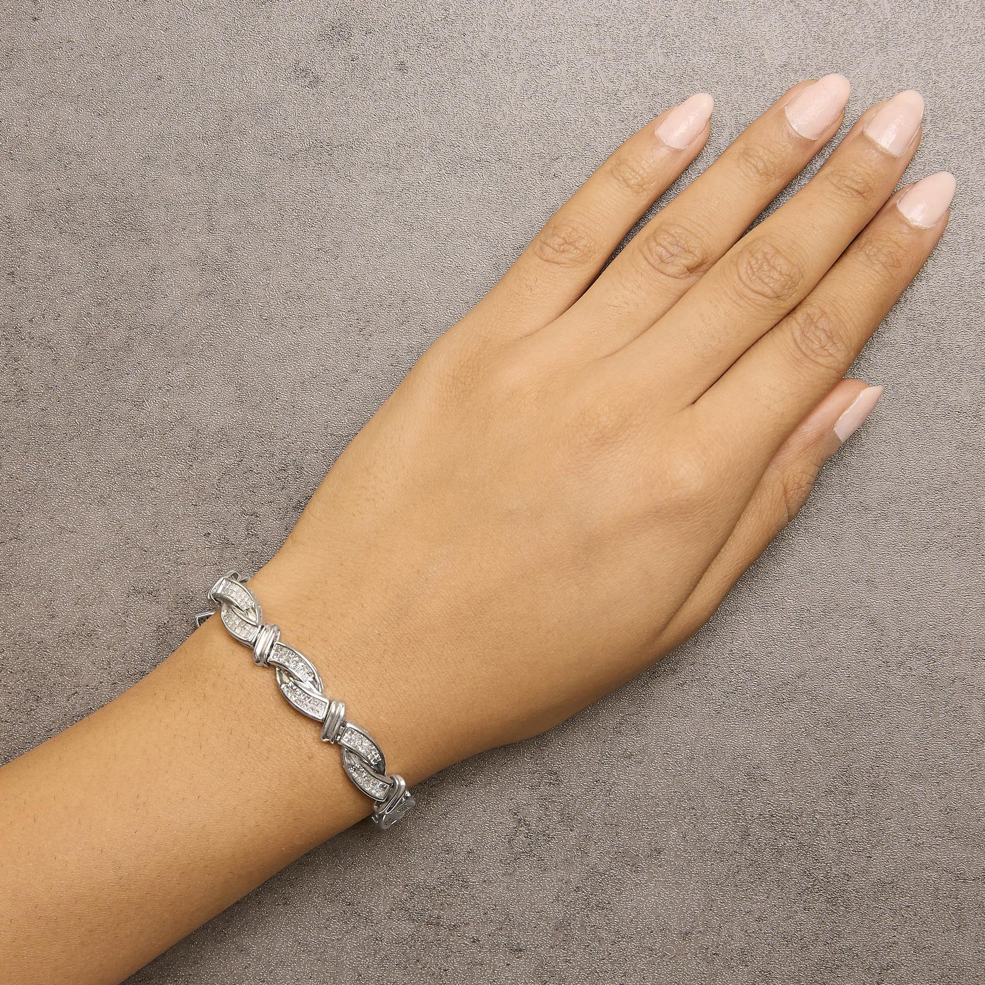 White metal bracelet with linked curved segments accented with white gemstones in invisible setting, shown on a model's wrist from a top angle.