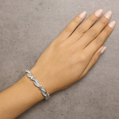 White metal bracelet with linked curved segments accented with white gemstones in invisible setting, shown on a model's wrist from a top angle.