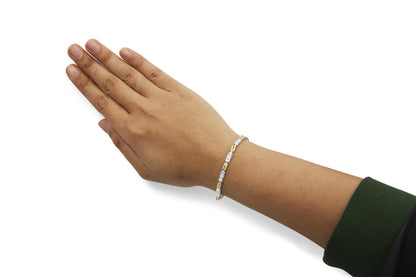 Two-toned bracelet with rectangular sections set with white gemstones in an invisible setting, worn on a model's wrist, shot from the side at an angle.