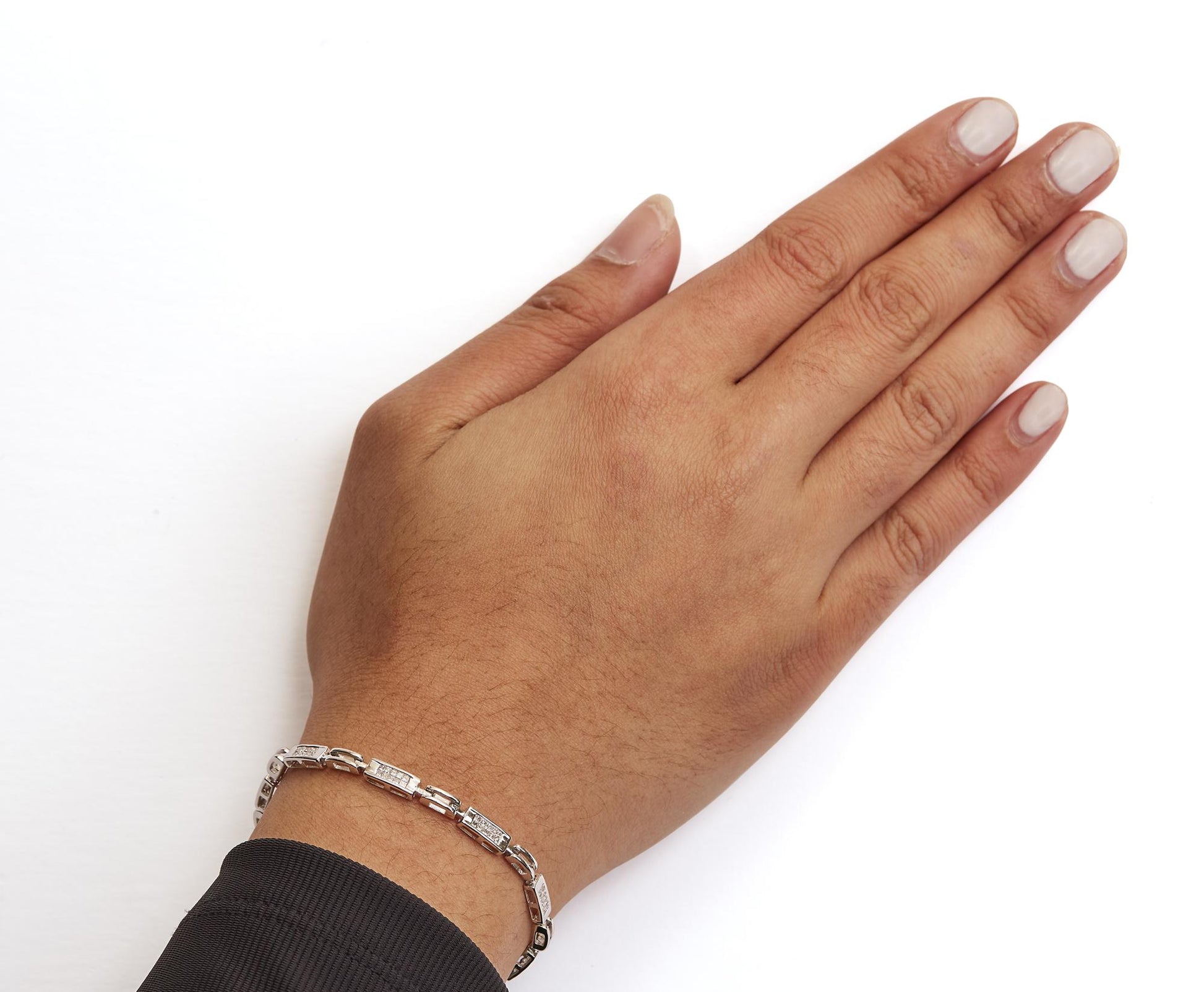 Close-up top view of a model's hand wearing a white metal bracelet with rectangular links set with small white gemstones in invisible settings.
