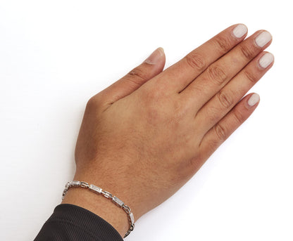 Close-up top view of a model's hand wearing a white metal bracelet with rectangular links set with small white gemstones in invisible settings.