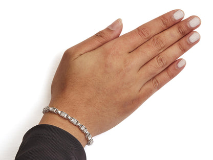 White metal bracelet with channel set princess-shaped white gemstones, worn on wrist, top-down angle.
