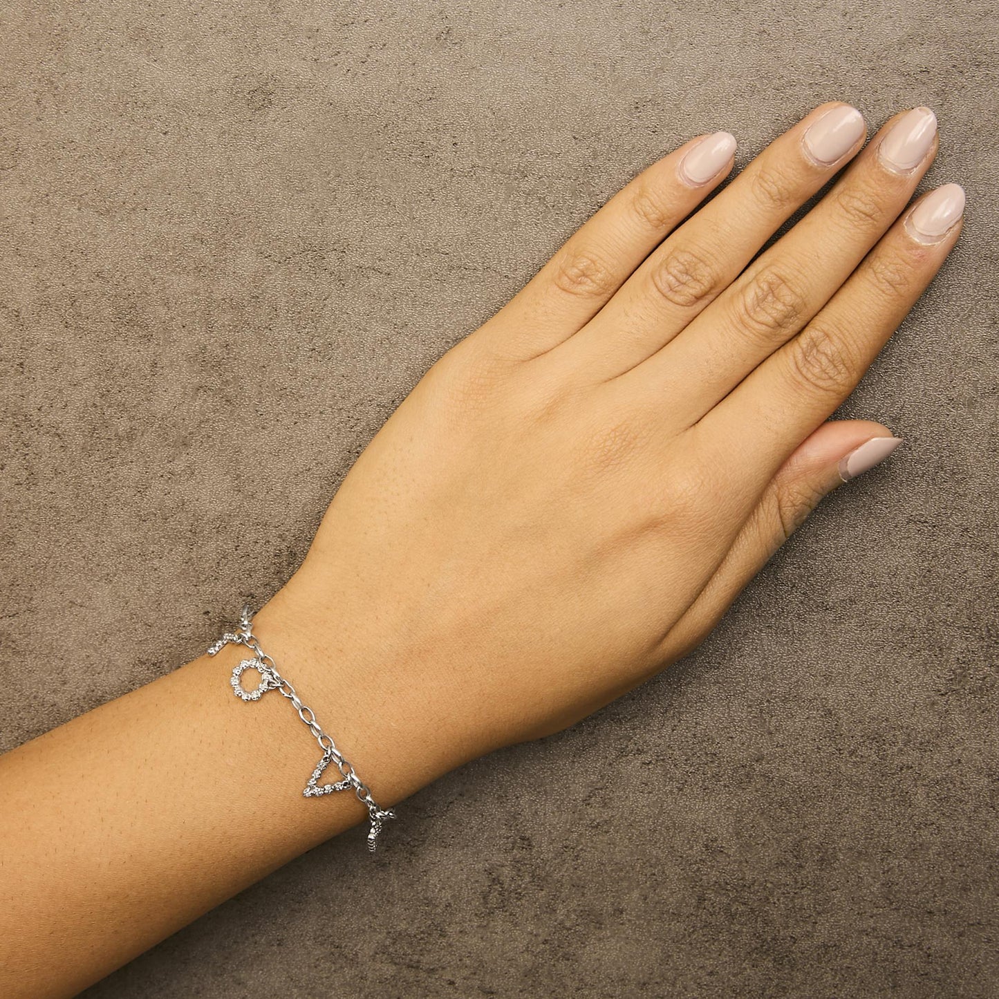 Top-down angle of a white metal bracelet with round white gemstones in micro-pave setting forming shaped charms, worn on a model's wrist.