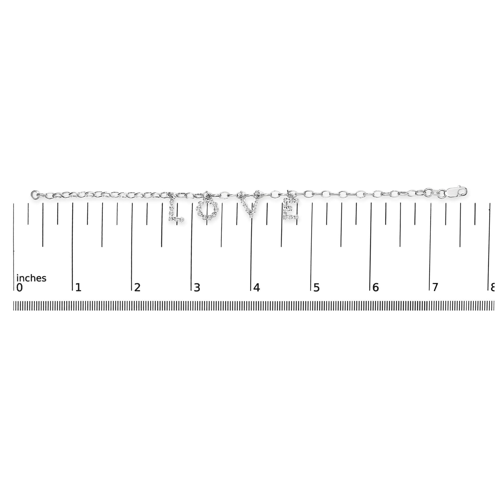 White metal bracelet with charms spelling 'LOVE' set with round white gemstones, shown flat on a ruler for size reference, top-down angle.