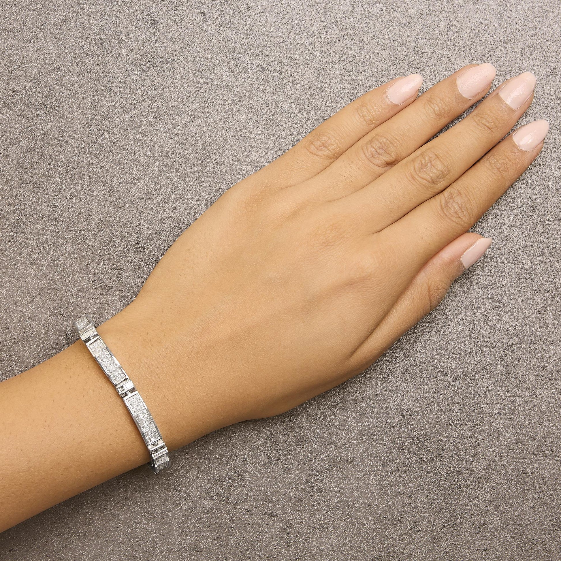 White metal bracelet with rectangular segments featuring baguette and square shaped white gemstones, shown worn on a model's wrist, top down angle.