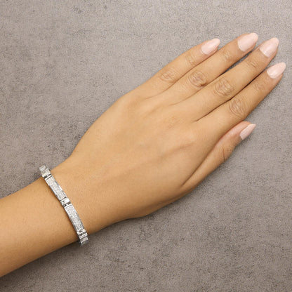 White metal bracelet with rectangular segments featuring baguette and square shaped white gemstones, shown worn on a model's wrist, top down angle.