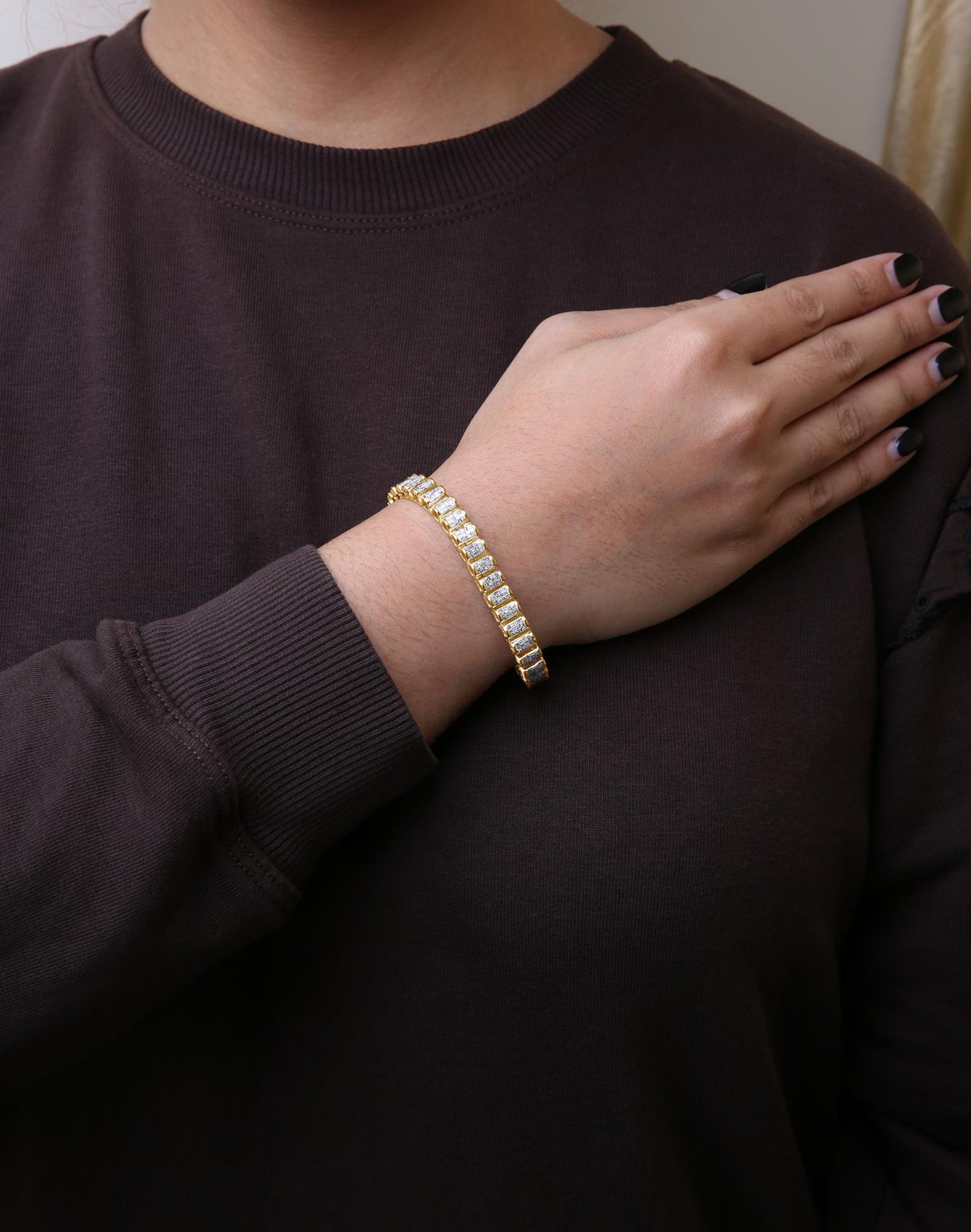 Yellow metal bracelet with white princess shape gemstones in invisible setting, worn on wrist, shot from front angle.