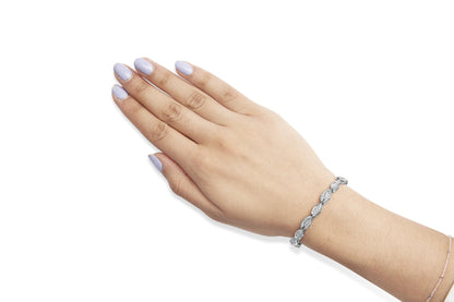 White metal bracelet with alternating oval links featuring round and baguette white gemstones, worn on wrist, top-down angle.