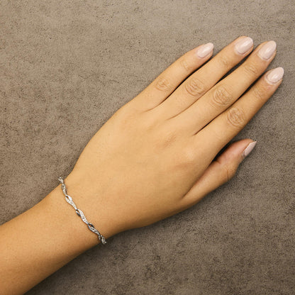 White metal bracelet with intertwined design and prong-set round white gemstones, shown on a model's wrist from above.