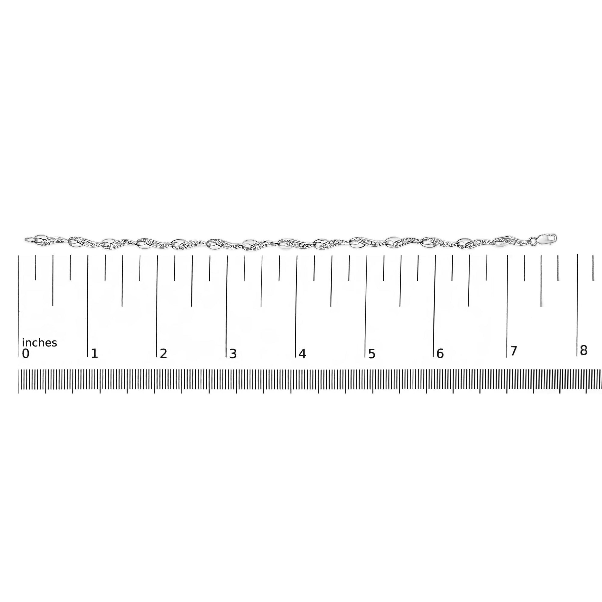 White metal bracelet with alternating loop and curved links set with round white gemstones in prong settings, laid flat on a ruler for size reference, shot from above.