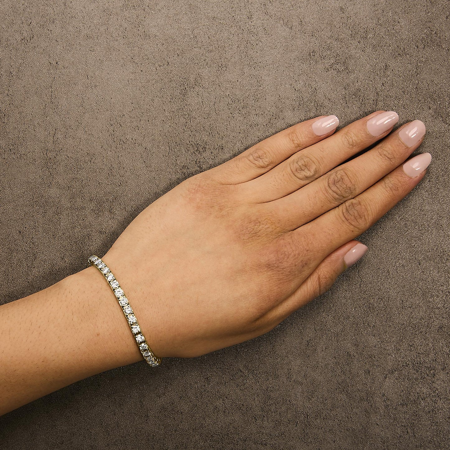 Close-up side angle of a hand model wearing a yellow metal bracelet featuring round white gemstones in prong settings.