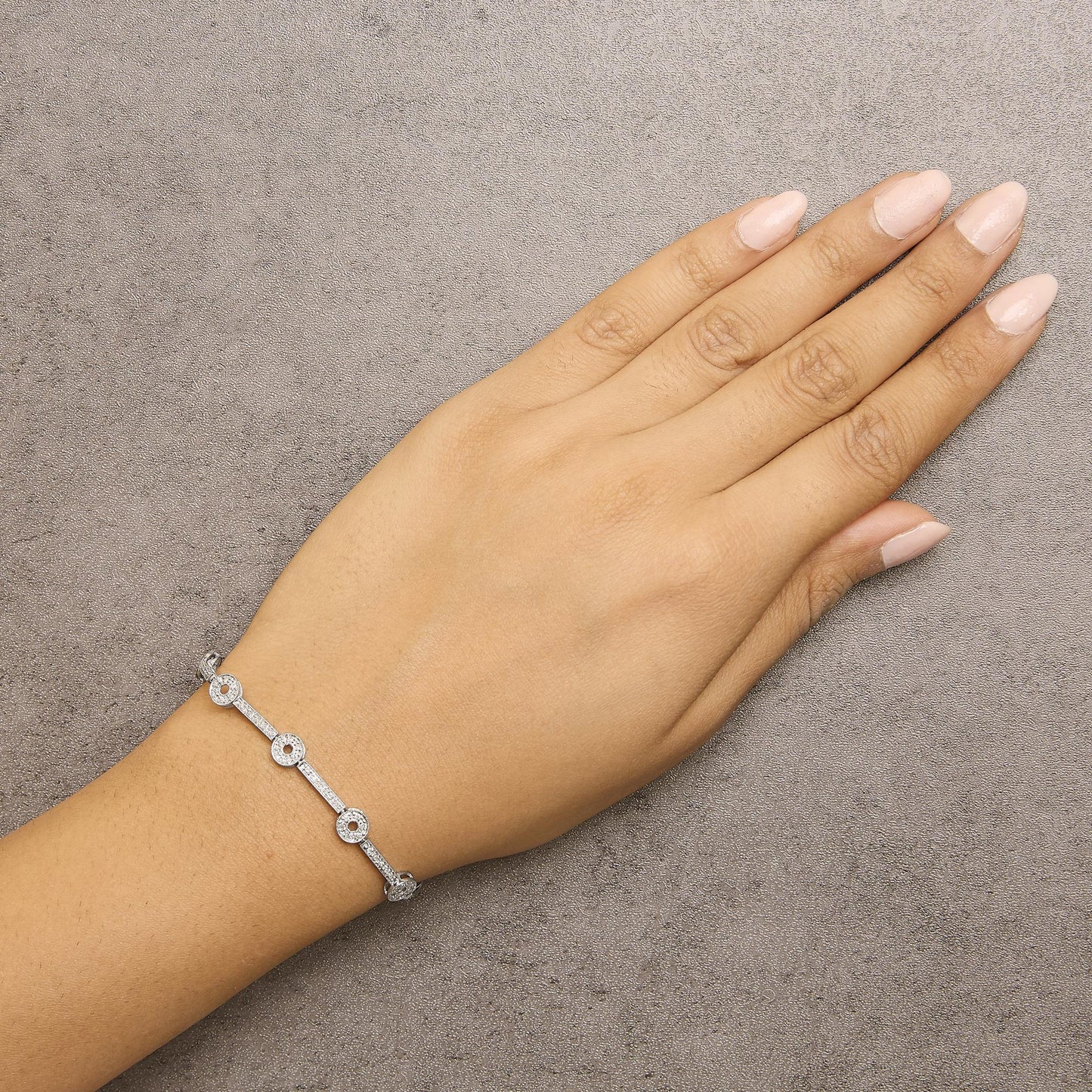 White metal bracelet with round white gemstones in prong settings, displayed on a model's wrist, shot from above.