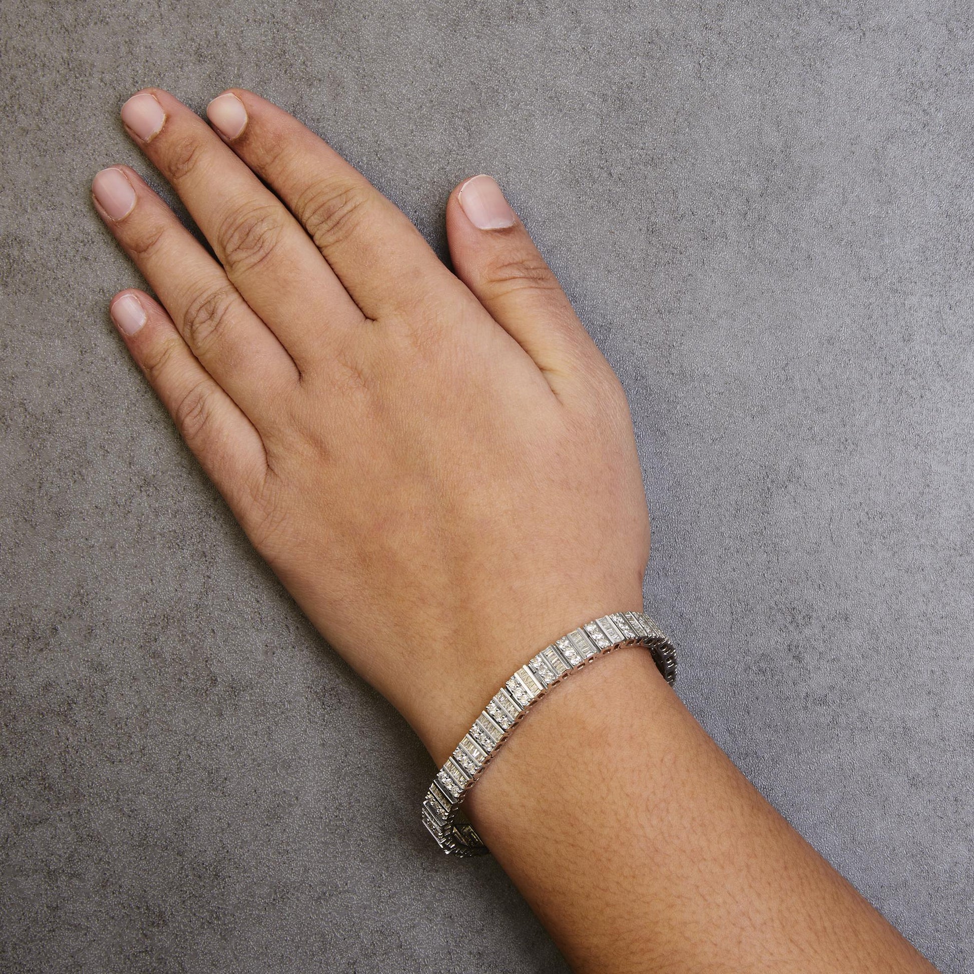 White metal bracelet with alternating rows of round prong-set and baguette channel-set white gemstones, shown on a model's wrist from above.