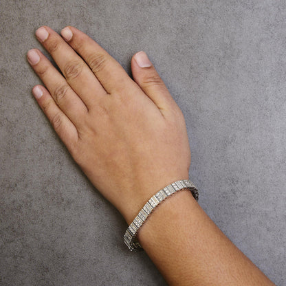 White metal bracelet with alternating rows of round prong-set and baguette channel-set white gemstones, shown on a model's wrist from above.