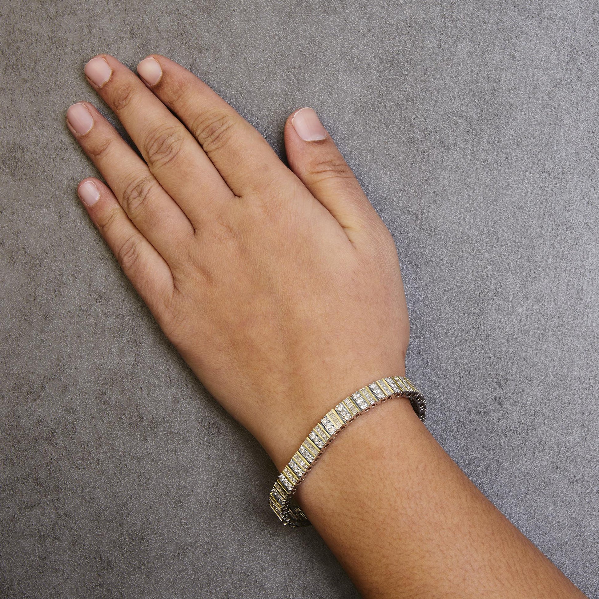 Yellow metal bracelet with white round and baguette gemstones, worn on a model's wrist, top-down angle.