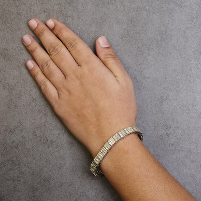 Yellow metal bracelet with white round and baguette gemstones, worn on a model's wrist, top-down angle.