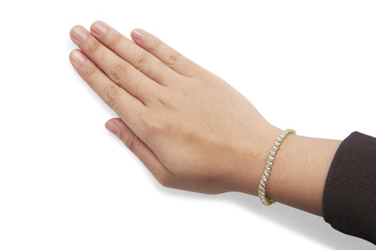 Yellow metal bracelet with round white gemstones in prong settings, worn on a model’s wrist, shot from above and slightly angled.