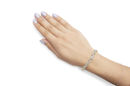 Close-up side angle of a yellow metal bracelet with white round and baguette gemstones in prong and channel settings, worn on a model's wrist.