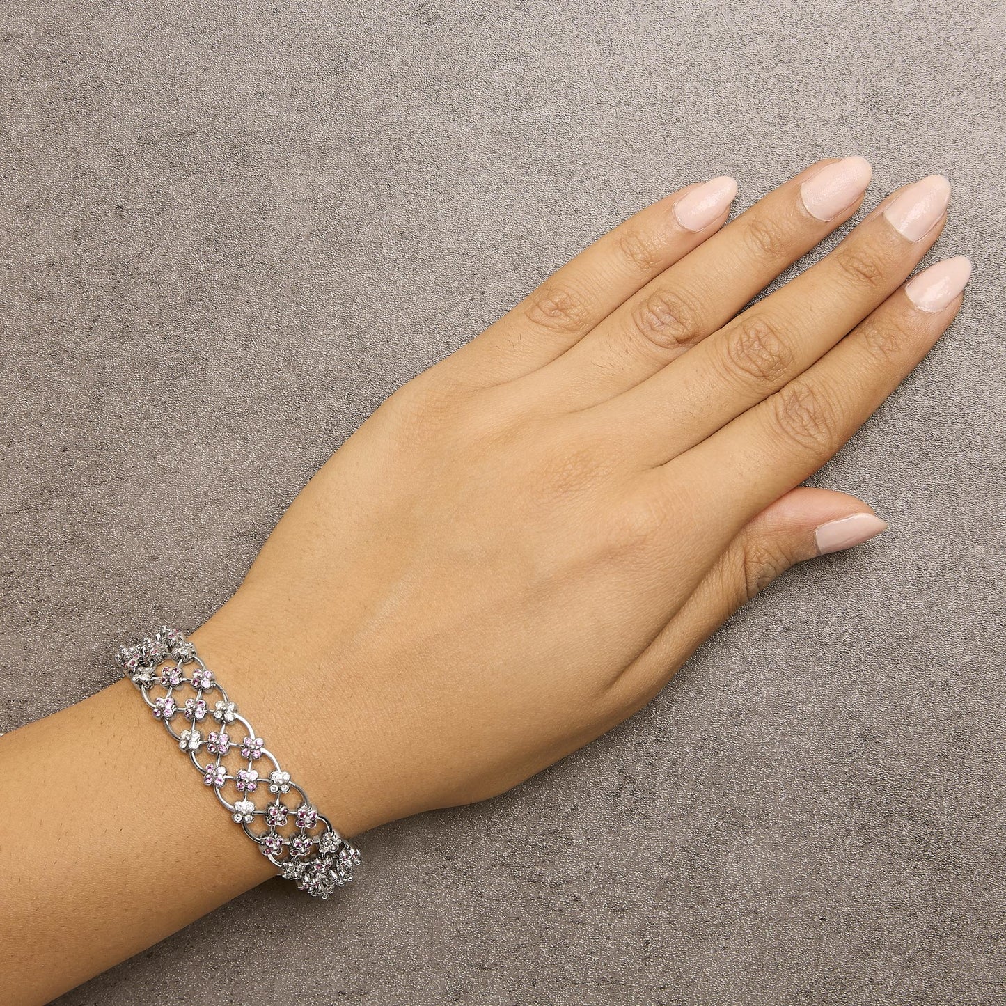 Bracelet with white metal lattice design adorned with pink and white round gemstones in bezel settings, shown on a model's wrist from a top angle.