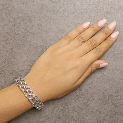 Bracelet with white metal lattice design adorned with pink and white round gemstones in bezel settings, shown on a model's wrist from a top angle.