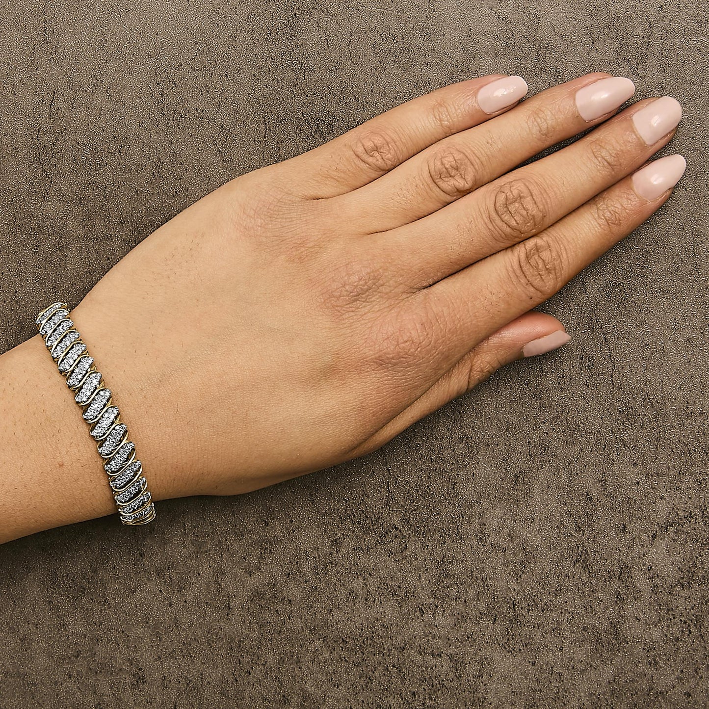 Yellow metal bracelet with white round gemstones in prong setting, worn on wrist of a hand with light pink nail polish, shown from top angle.