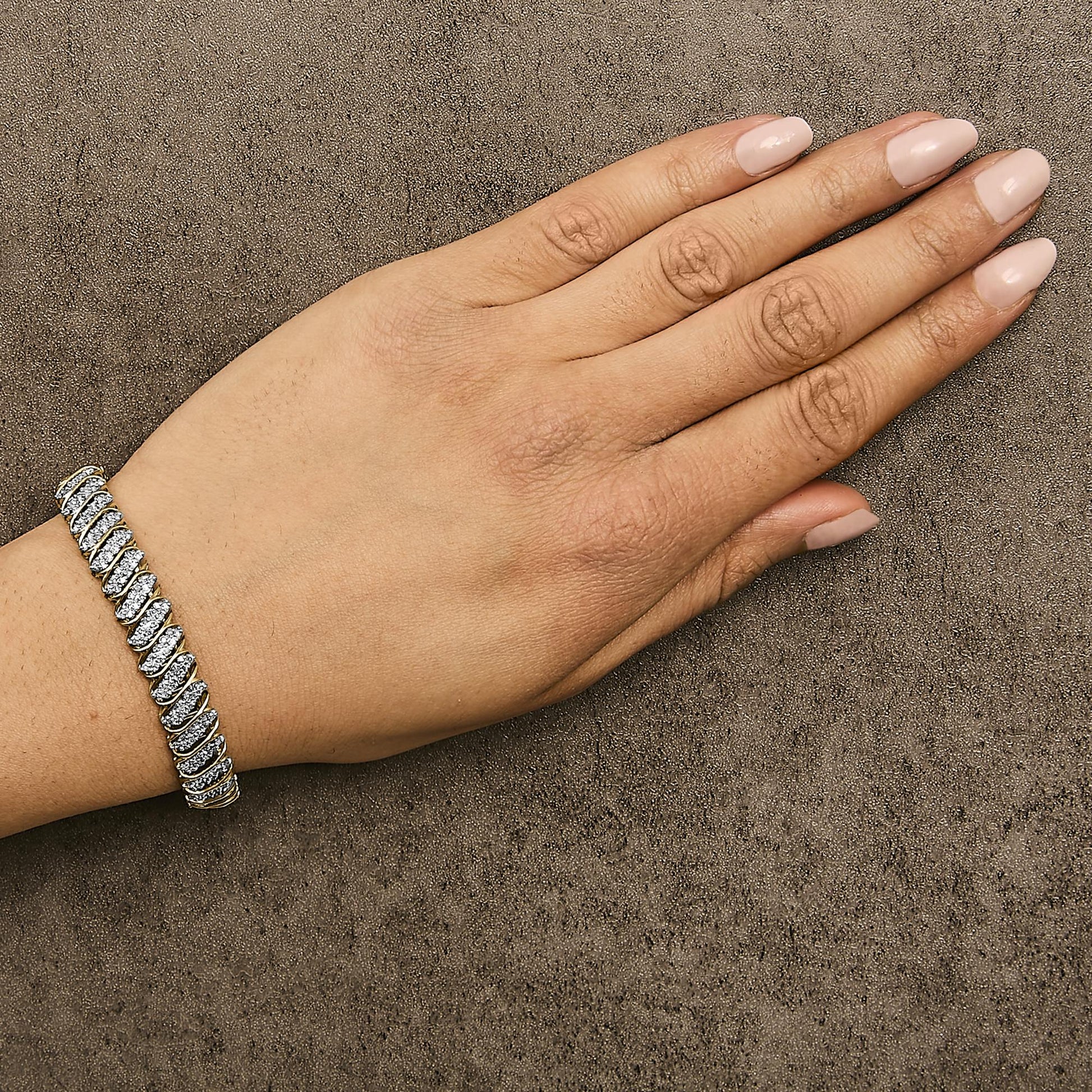 Yellow metal bracelet with white round gemstones in prong setting, worn on wrist of a hand with light pink nail polish, shown from top angle.
