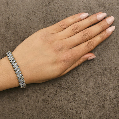 Yellow metal bracelet with white round gemstones in prong setting, worn on wrist of a hand with light pink nail polish, shown from top angle.