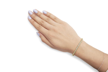 Yellow metal bracelet with round white gemstones in prong setting, shown on model's wrist from top angle.