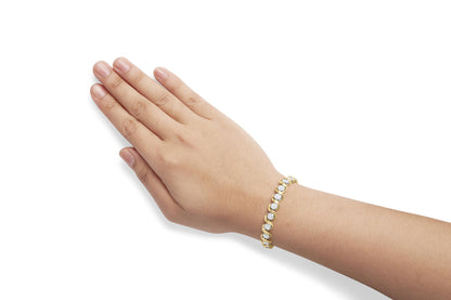 Yellow metal bracelet with round white gemstones in prong settings, shown on a model's wrist, angled from above.