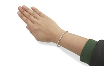 Close-up side angle of a wrist on a model wearing a yellow and white metal bracelet with alternating round white gemstones in prong settings.