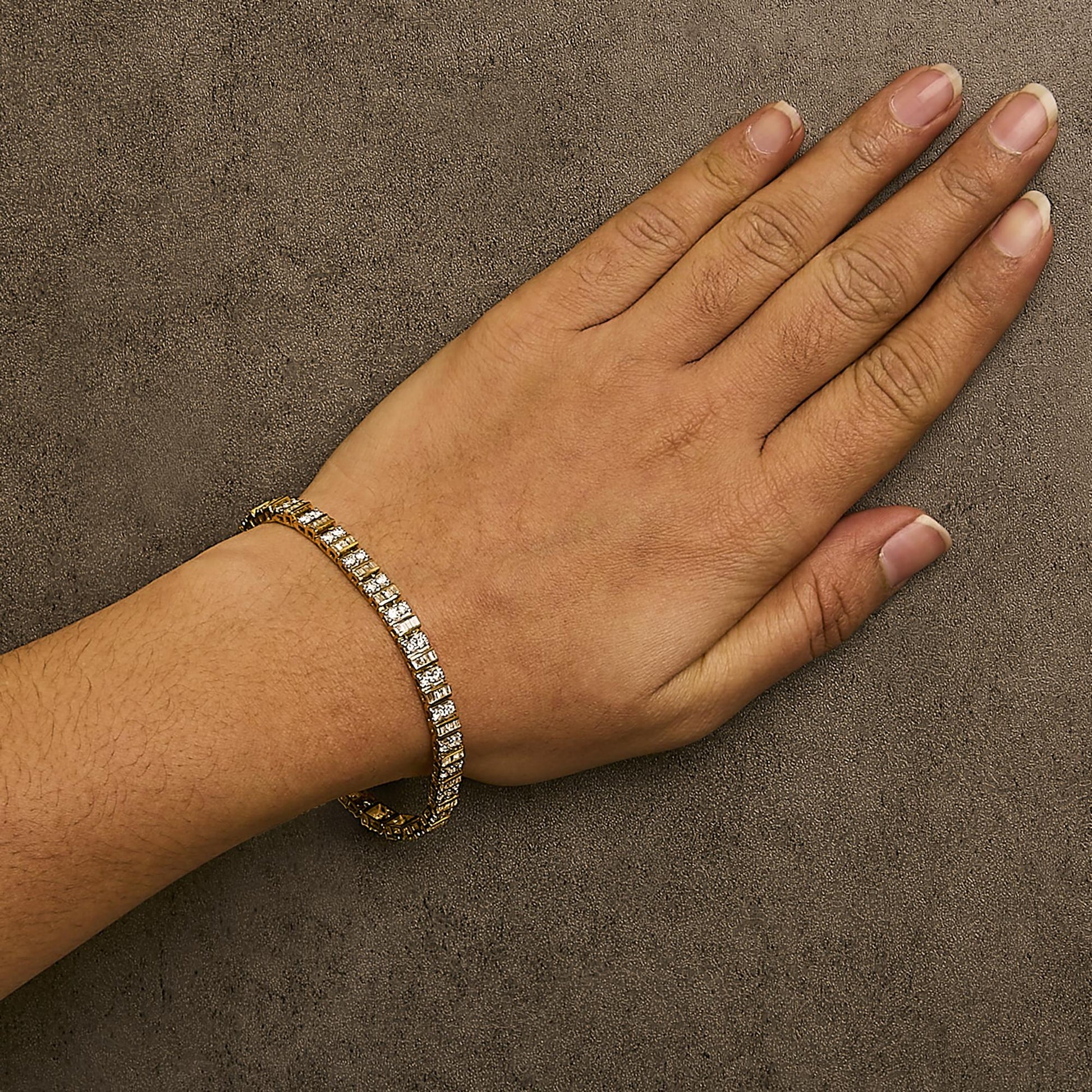 Yellow metal bracelet with alternating round white gemstones in prong settings and baguette white gemstones in channel settings, shown on a model's wrist from a top angle.