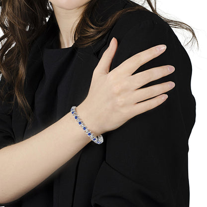 White metal bracelet with alternating round blue and white gemstones in prong and miracle settings, shown on a model's wrist from a side angle.