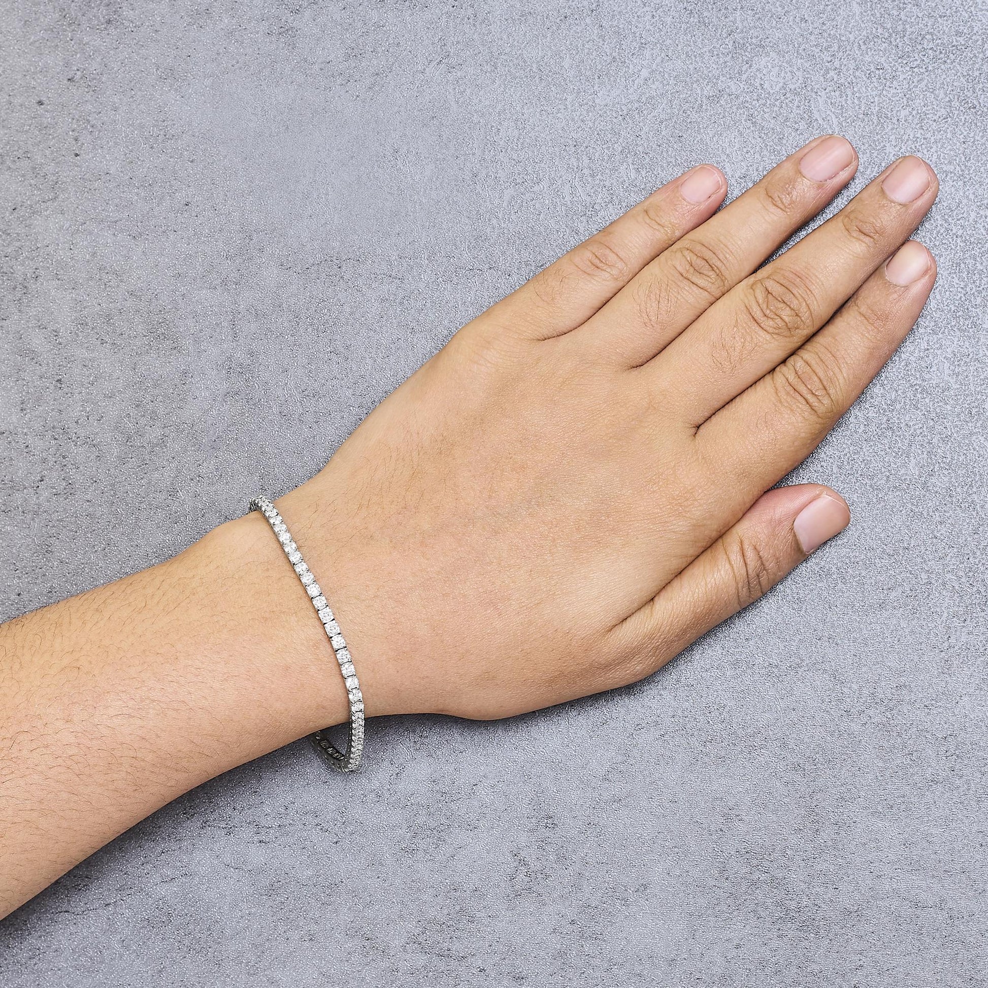 White metal bracelet with round white gemstones in prong settings, worn on a model's wrist, top-down angle.