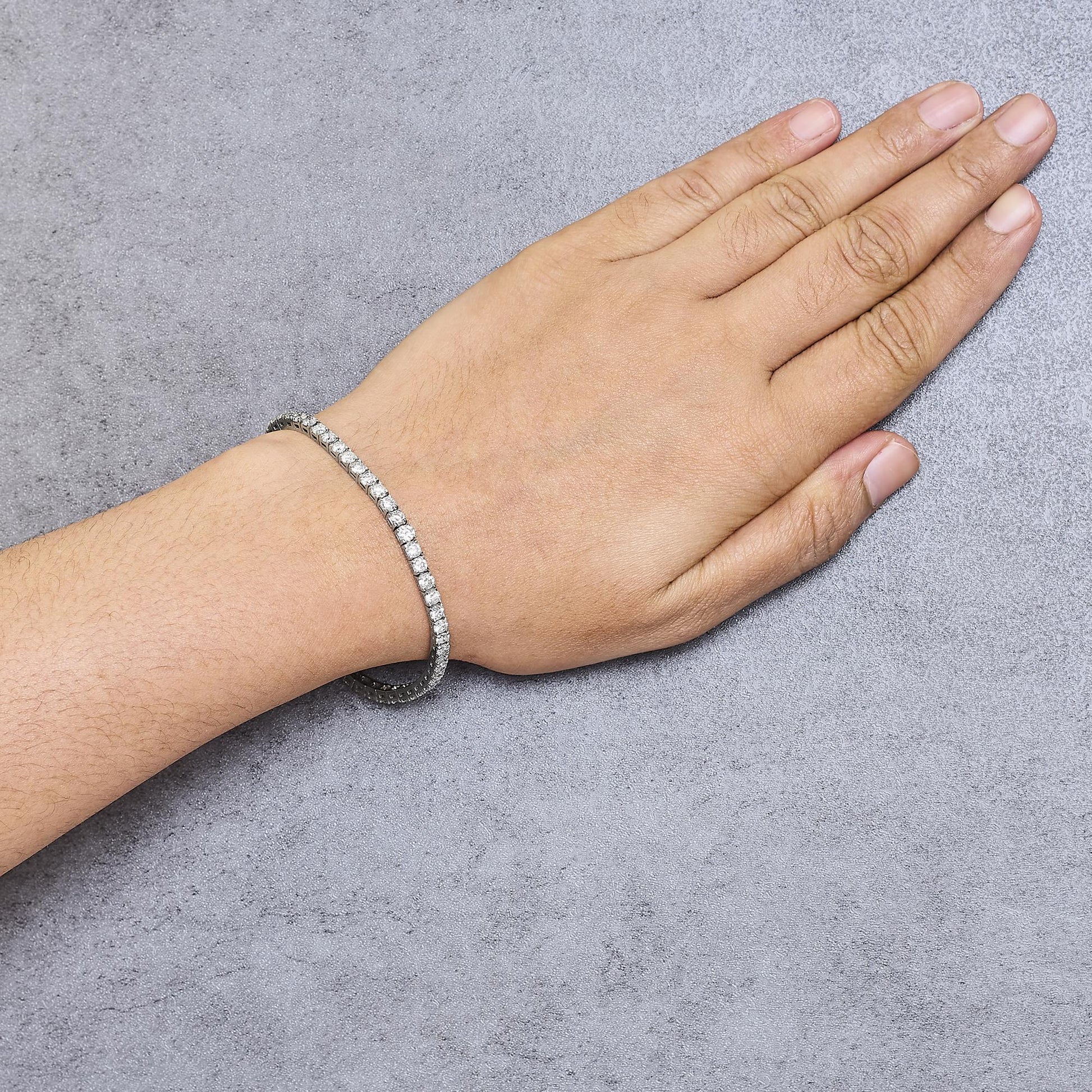 White metal bracelet with round prong-set white gemstones, worn on wrist, shot from above.