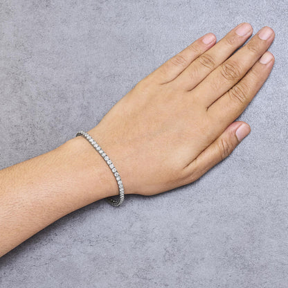 White metal bracelet with round white gemstones in prong settings, worn on a model's wrist, top-down angle.