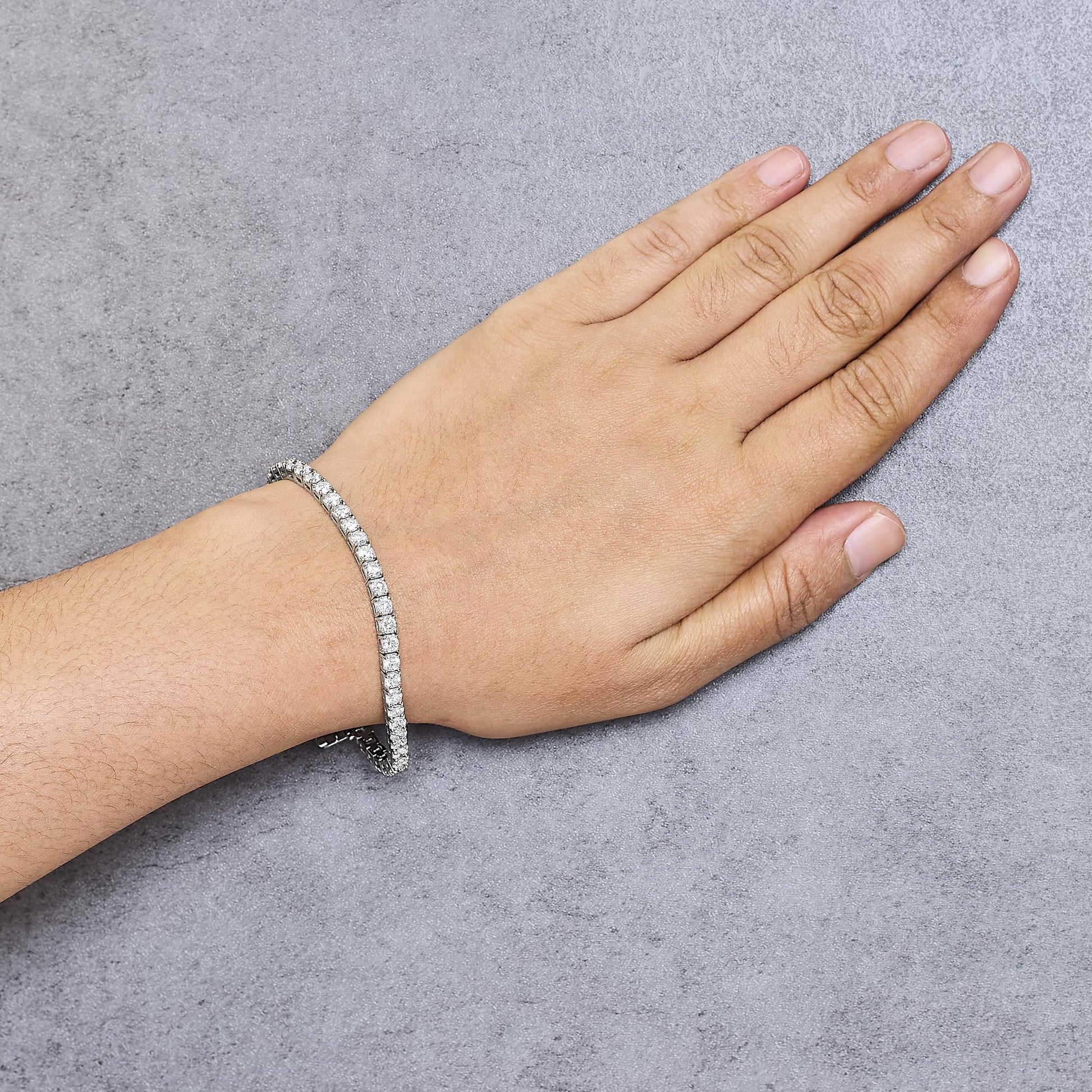 White metal bracelet with prong-set round white gemstones, shown on a wrist from a top-down angle.
