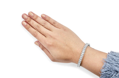Close-up angled view of a hand wearing a white metal bracelet featuring a row of square-shaped white gemstones in an invisible setting.