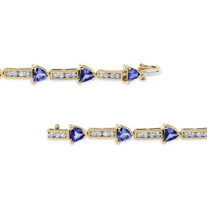 Close-up image of a yellow metal bracelet with alternating sections of round white gemstones in channel settings and blue trillion-shaped gemstones in prong settings, shown from a side angle.