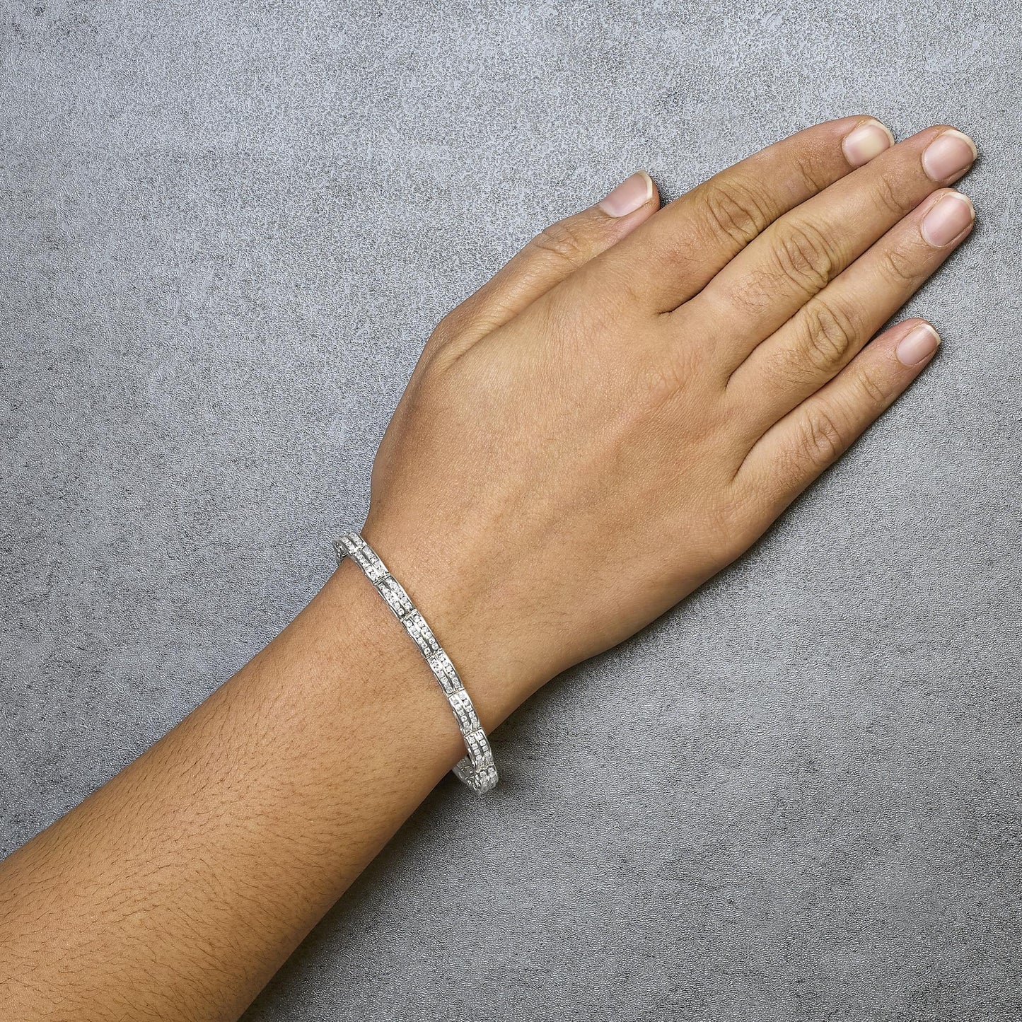 White metal bracelet with channel-set round white gemstones, shown on the wrist from an overhead angle.