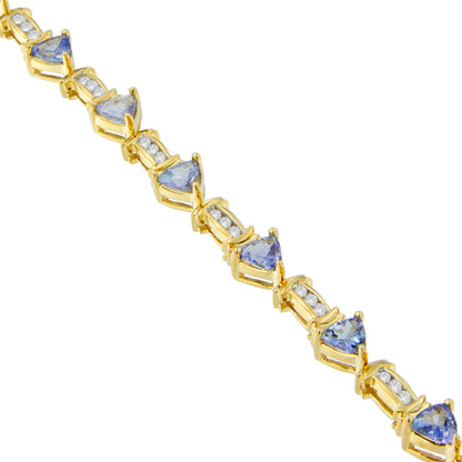 Diagonal close-up of a yellow metal bracelet featuring alternating triangular blue gemstones in prong settings and clusters of round white gemstones in channel settings.